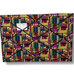 Peut inclure: Un tableau d'affichage en tissu coloré avec un motif géométrique dans des tons de rouge, vert, jaune, bleu et violet. Le tableau est divisé en sections par un ruban bleu marine et comporte des punaises dorées.