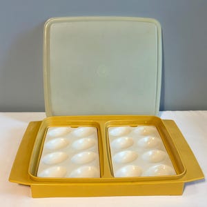 May include: A vintage yellow plastic deviled egg carrier with a matching lid. The carrier has two compartments, each holding six egg-shaped indentations. The lid is a light green color.