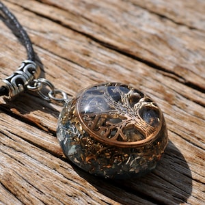 Puede incluir: Un colgante redondo de cristal transparente con un dise&ntilde;o de &aacute;rbol de la vida dorado. El colgante est&aacute; en un cord&oacute;n de cuero negro con un cierre plateado.