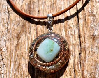 May include: A round pendant necklace featuring a central light green stone encased in clear resin with embedded copper wire coils and gold-colored metal flakes. The pendant hangs from a smooth brown leather cord with a silver-toned metal bail.