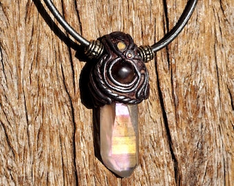 May include: A pendant necklace featuring a clear, iridescent crystal point suspended from a dark leather cord. The crystal is encased in a dark, textured, sculpted setting with a central dark bead and two small metallic beads on the cord.