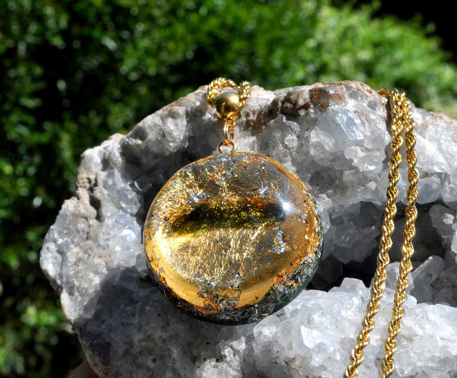Moldavite Orgonite necklace with 24k gold flakes in resin on gold chain, displayed on raw quartz crystal.