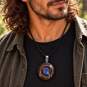 Peut inclure: Un pendentif circulaire avec une pierre centrale en lapis-lazuli bleu entourée d'un anneau en fil de cuivre torsadé, le tout enchâssé dans une base en résine sombre avec des éclats métalliques, suspendu à un cordon noir avec une bélière argentée.