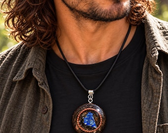 May include: A circular pendant featuring a central blue lapis lazuli stone surrounded by a coiled copper wire ring, all encased in a dark resin base with metallic flecks. The pendant hangs from a simple black cord necklace with a silver-toned bail.