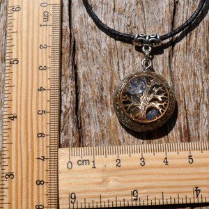 Puede incluir: Un collar con un colgante de &aacute;rbol de la vida de plata y oro con un cord&oacute;n negro. El colgante es redondo y tiene una cubierta de resina transparente con escamas doradas y plateadas en el interior. El colgante mide aproximadamente 2,5 cm de di&aacute;metro.