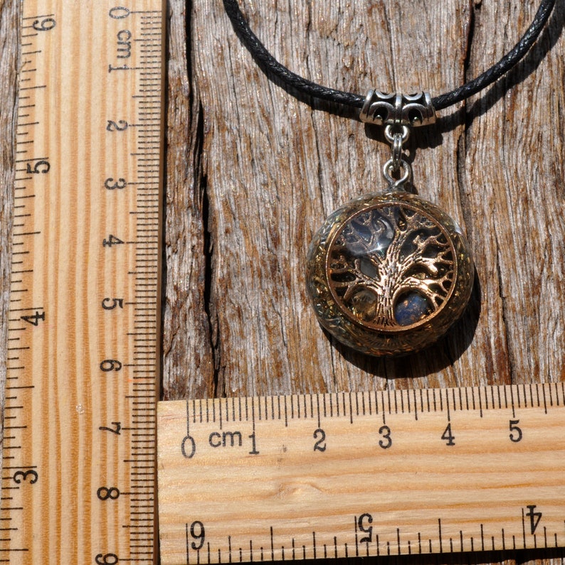 Puede incluir: Un collar con un colgante de &aacute;rbol de la vida de plata y oro con un cord&oacute;n negro. El colgante es redondo y tiene una cubierta de resina transparente con escamas doradas y plateadas en el interior. El colgante mide aproximadamente 2,5 cm de di&aacute;metro.