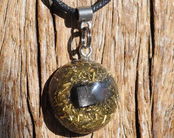 May include: A spherical pendant necklace featuring a clear resin dome filled with gold-colored metallic shavings and a single dark, opaque stone fragment at the center. The pendant is attached to a black cord by a silver-toned metal bail and ring.