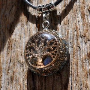 This lovely 2.6 cm / 1" in diameter orgone pendant contains various metal shavings, clear Quartz, Rhodizite, Selenite. The main stone is a flash Labradorite in the front behind a Silver Tree of of Life symbol. Comes on adjustable cotton cord.