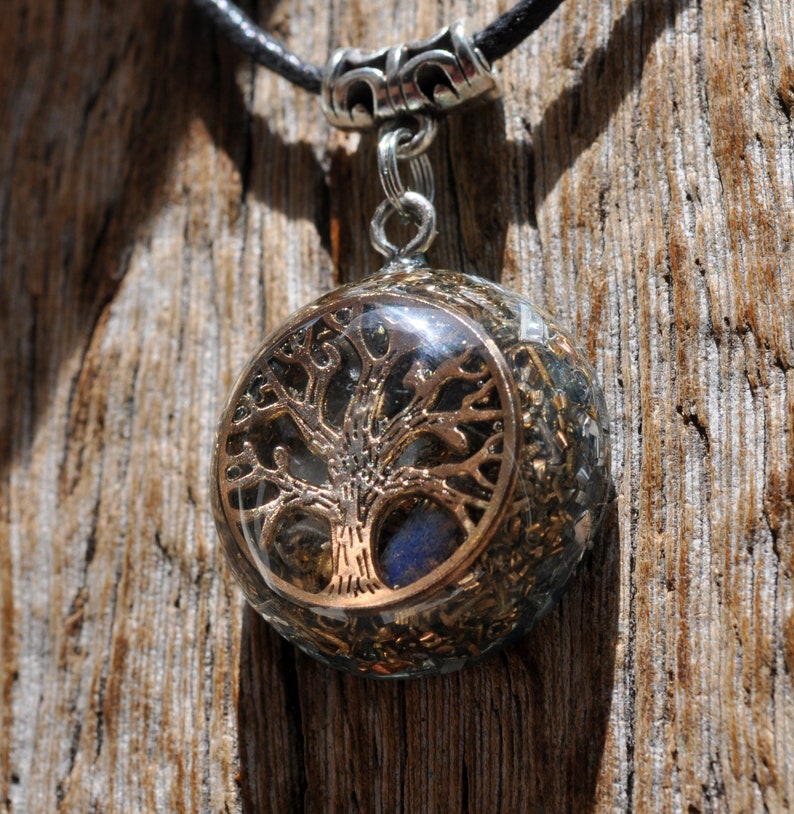 This lovely 2.6 cm / 1" in diameter orgone pendant contains various metal shavings, clear Quartz, Rhodizite, Selenite. The main stone is a flash Labradorite in the front behind a Silver Tree of of Life symbol. Comes on adjustable cotton cord.