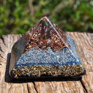 May include: A pyramid-shaped resin sculpture featuring a central iridescent crystal point surrounded by layers of embedded copper shavings, silver-colored metal fragments, and a base layer of gold-toned metal shavings within a clear, smooth finish.