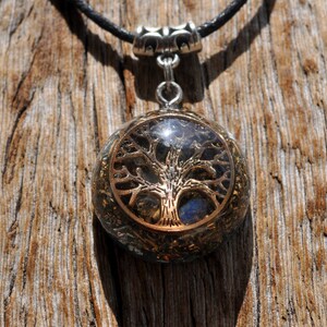 Puede incluir: Un collar con un colgante redondo de resina transparente que contiene un dise&ntilde;o de &aacute;rbol de la vida dorado y cristales azules y plateados. El collar est&aacute; en un cord&oacute;n negro.