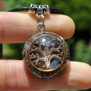 Puede incluir: Un collar con un colgante de plata, que consiste en una esfera transparente que contiene un dise&ntilde;o de &aacute;rbol de la vida dorado. La esfera est&aacute; rodeada de peque&ntilde;os cristales y piedras.