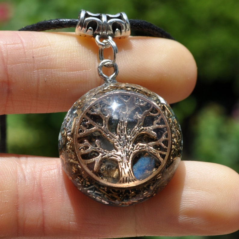 Puede incluir: Un collar con un colgante de plata, que consiste en una esfera transparente que contiene un dise&ntilde;o de &aacute;rbol de la vida dorado. La esfera est&aacute; rodeada de peque&ntilde;os cristales y piedras.