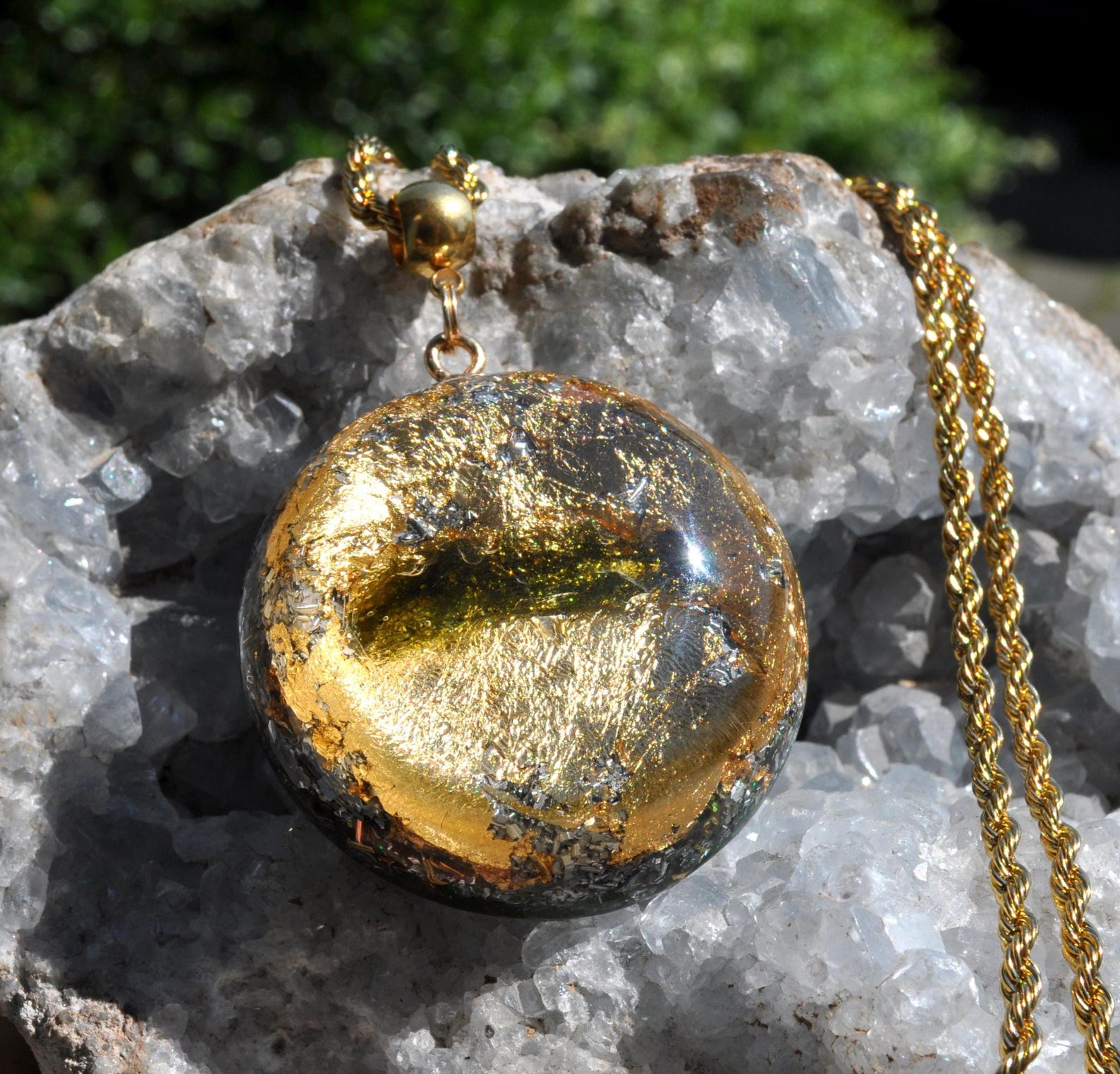 Moldavite Orgonite necklace with 24k gold flakes in resin on gold chain, displayed on raw quartz crystal.