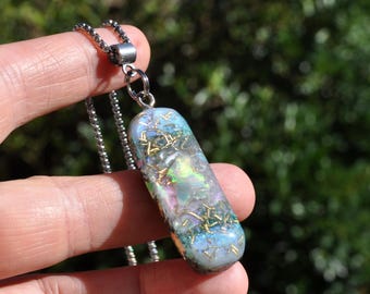 May include: A rectangular pendant necklace featuring a translucent resin base with embedded iridescent flakes, shimmering blue and purple hues, and fine gold-colored metallic wire accents, suspended from a silver-toned metal ball chain.