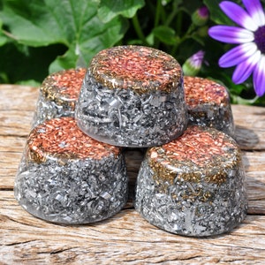 Peut inclure: Cinq objets en forme de dôme avec une base en résine transparente, remplis de copeaux de métal argenté. Les dessus sont un mélange de métal cuivré et doré. Les objets sont disposés sur une surface en bois, avec un feuillage vert et une fleur violette en arrière-plan.