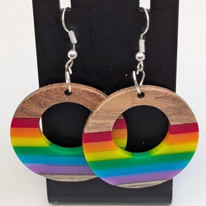 May include: A pair of hoop earrings with a wooden outer ring and a rainbow-colored inner ring. The earrings have silver-colored hooks. The rainbow colors are red, orange, yellow, green, blue, and purple.