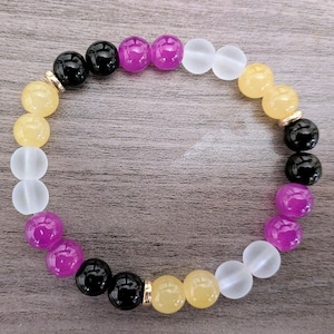 May include: A beaded bracelet featuring a variety of colorful beads. The bracelet includes yellow, white, black, and purple beads. The beads are strung together with a gold-colored spacer.