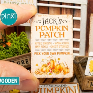 May include: A wooden sign with a white background and brown trim. The sign reads "Jack's Pumpkin Patch" with the text "Apple Bobbing, Warm Cider, Hay Rides, Ghost Stories, Pick Your Own Pumpkin" underneath. The sign is decorated with a watercolor illustration of pumpkins and sunflowers.