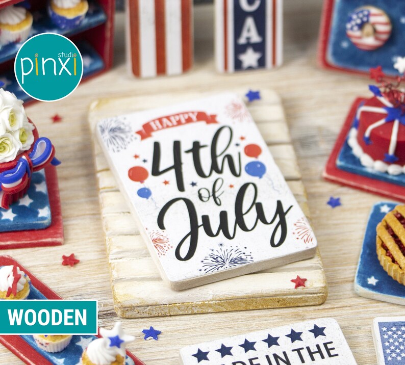 May include: A white wooden sign with the text "Happy 4th of July" in black lettering. The sign is decorated with red, white, and blue stars and fireworks. The sign is sitting on a white wooden surface.