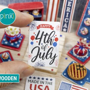 May include: Wooden sign with the text "Happy 4th of July" in black lettering with red, white, and blue stars and fireworks. The sign is on a wooden surface with other miniature patriotic decorations.