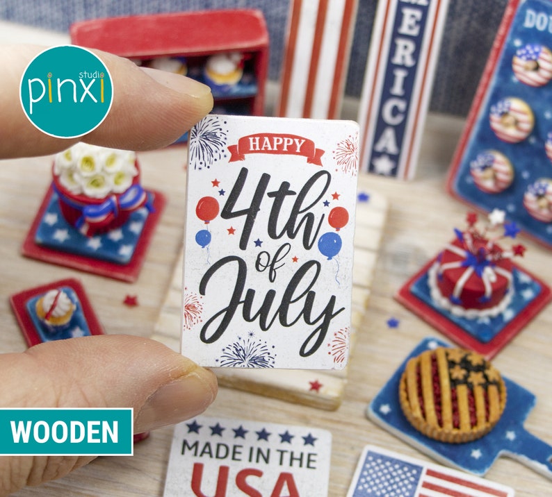 May include: Wooden sign with the text "Happy 4th of July" in black lettering with red, white, and blue stars and fireworks. The sign is on a wooden surface with other miniature patriotic decorations.