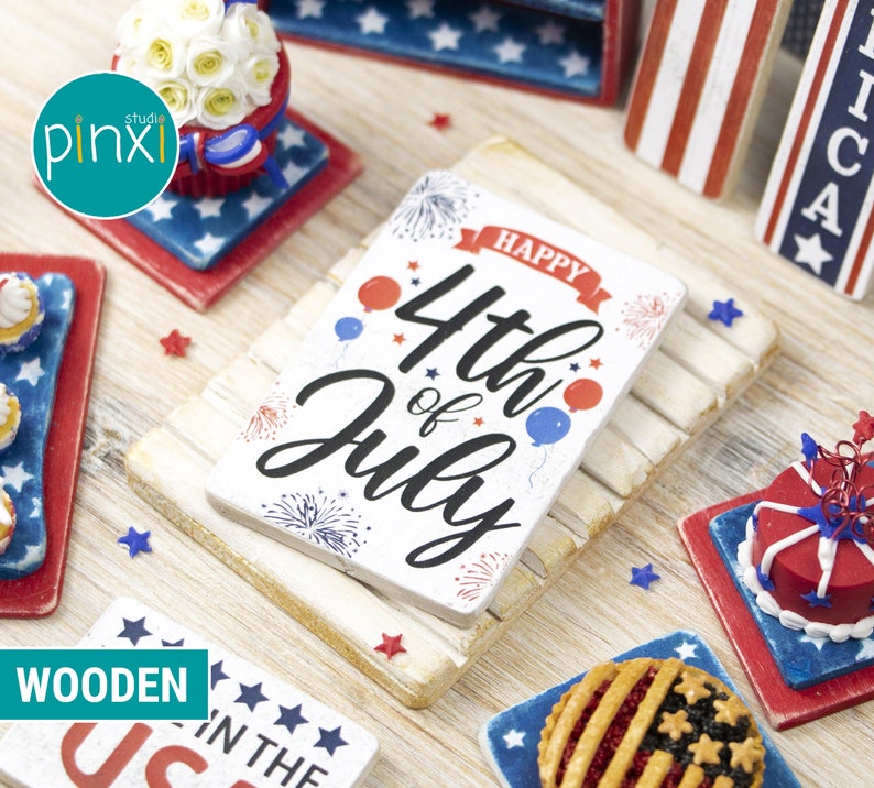 May include: A miniature wooden sign with the text "Happy 4th of July" in red, white, and blue. The sign is decorated with fireworks, stars, and balloons. The sign is on a white wooden surface with other miniature patriotic decorations.