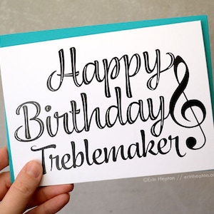 May include: A white card with a teal border. The card has black text that says "Happy Birthday Treblemaker" with a treble clef symbol.