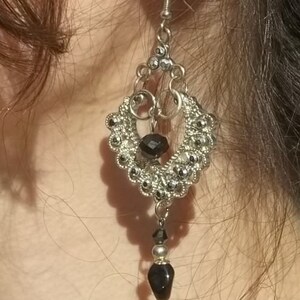May include: Silver dangle earrings with black beads. The earrings have a teardrop shape and are accented with small, round beads.
