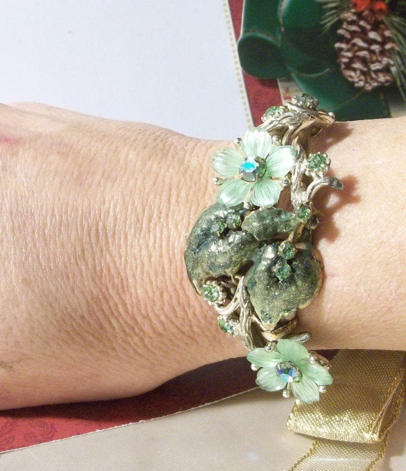 Pode incluir: Um bracelete vintage verde e dourado com um design floral. O bracelete apresenta um grupo de flores verdes com strass no centro. O bracelete &eacute; feito de metal e tem um visual delicado e feminino.