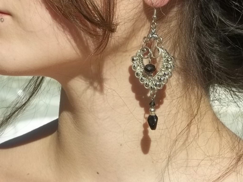 May include: Silver dangle earrings with black beads. The earrings have a teardrop shape and are accented with small, round beads.