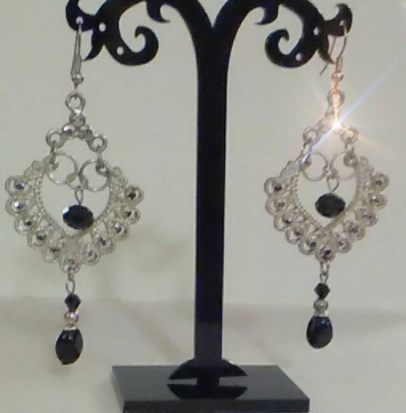 May include: A pair of silver dangle earrings with black beads. The earrings feature a delicate, intricate design with a heart shape at the center.