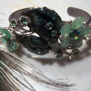 Pode incluir: Uma pulseira de prata com flores de vidro verde e transparente. A pulseira &eacute; decorada com folhas de prata e pedras.