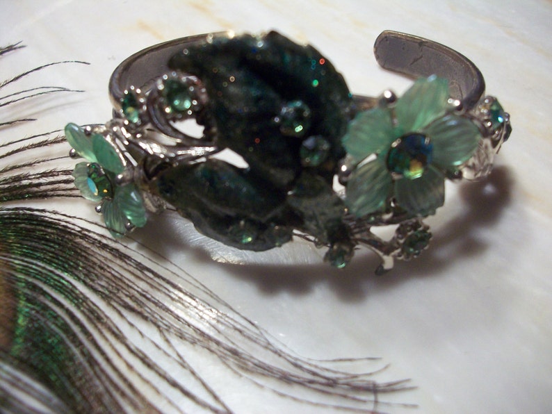 Pode incluir: Uma pulseira de prata com flores de vidro verde e transparente. A pulseira &eacute; decorada com folhas de prata e pedras.