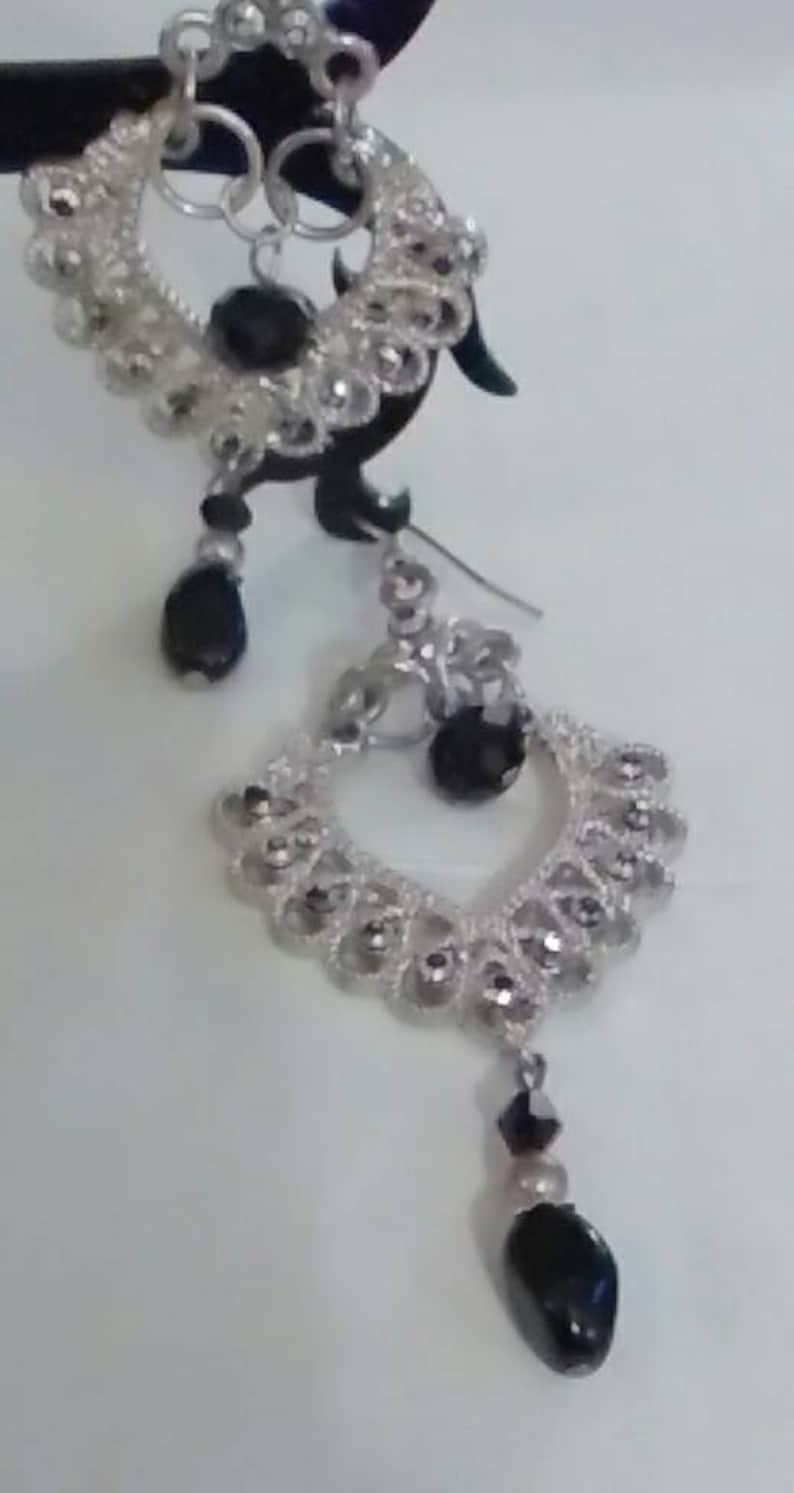 May include: Silver dangle earrings with black beads. The earrings feature a delicate, intricate design.