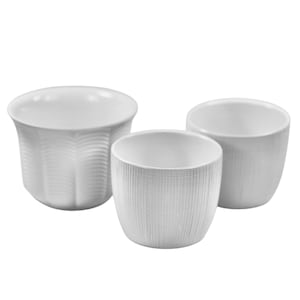 Può includere: Tre tazze in ceramica bianca con superfici strutturate. Le tazze variano in dimensioni e presentano diversi motivi, tra cui un design a onde e un motivo a tratteggio incrociato. Le tazze sono vuote e poste su uno sfondo bianco.