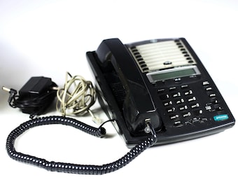 Pode incluir: Um telefone preto com fio, alto-falante, teclado e tela. O telefone tem um fio espiralado e um adaptador de energia.