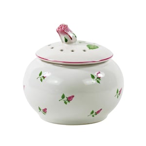 Puede incluir: Un tarro de cerámica blanco con tapa, adornado con pequeñas ilustraciones de rosas rosas y hojas verdes. La tapa tiene un borde rosa y un asa de capullo de rosa. El tarro tiene forma redonda y probablemente se utiliza para guardar o decorar.