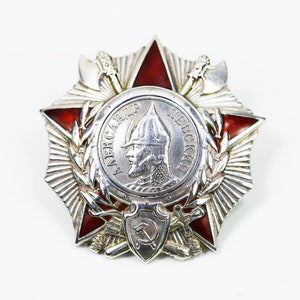 May include: A silver and red star-shaped medal with a central image of a man in a helmet and the text "АЛЕКСАНДР НЕВСКИЙ" around the image.