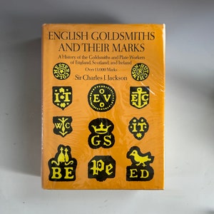 May include: A yellow book cover with the title "English Goldsmiths and Their Marks" and the subtitle "A History of the Goldsmiths and Plate Workers of England, Scotland, and Ireland. Over 13,000 Marks." The author is Sir Charles J. Jackson. The cover features several black and yellow illustrations of historical goldsmith marks.