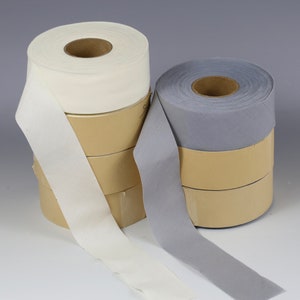 May include: Two rolls of fabric tape, one white and one gray, are stacked on top of cardboard spools. The white tape is on the left and the gray tape is on the right.