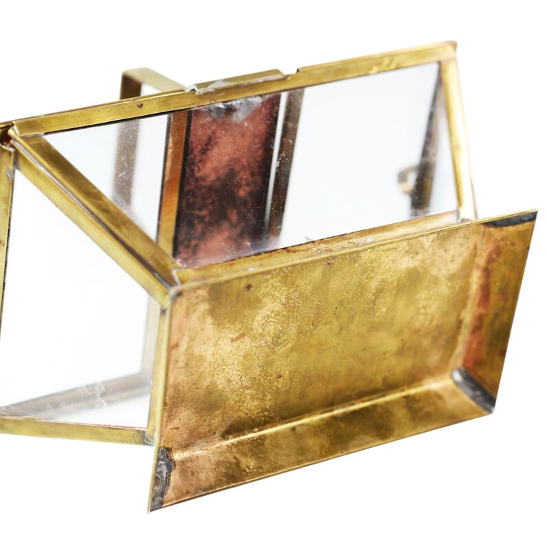 May include: A vintage brass box with a hinged lid and glass panels. The box has a rectangular shape with a tarnished, aged appearance. The glass panels are clear, and the box is open, revealing the interior.