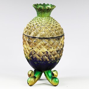 May include: A gold and green pineapple-shaped decorative jar with a blue base and three legs. The jar has a lid with a textured design.