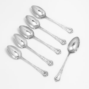 May include: Six silver spoons with ornate handles. The spoons are arranged in a fan shape on a white background.