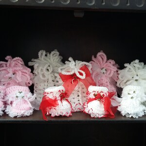Op de afbeelding: Set van zes gehaakte babyschoentjes in roze, wit en rood met kantversiering en lintaccenten.