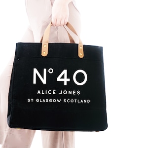 May include: A black canvas tote bag with brown leather handles and gold accents. The bag has the text "N&deg;40 ALICE JONES ST GLASGOW SCOTLAND" printed in white.