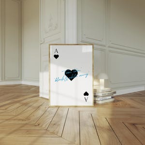 May include: A framed art print of the Ace of Hearts playing card. The card features a black heart, the letter "A", and the text "Toon town, black & white army" in a handwritten style. The frame is gold.