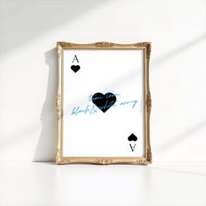 May include: A framed print featuring the Ace of Spades card design. The card has a black heart symbol and the letter "A" at the top and bottom. The text "toon toon black & white army" is written in blue and black script. The frame is gold.