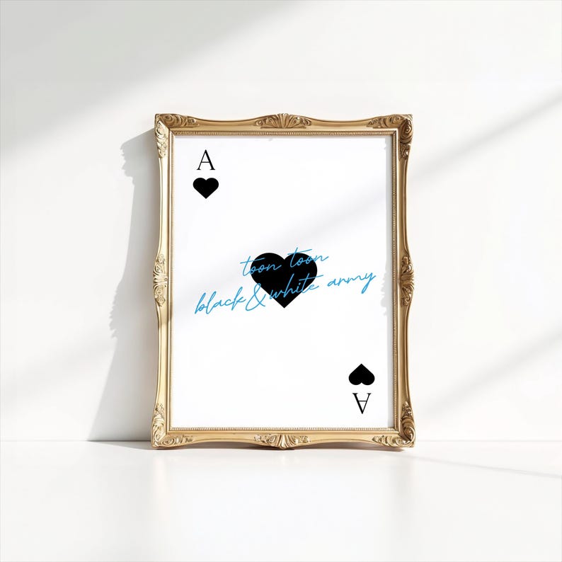 May include: A framed print featuring the Ace of Spades card design. The card has a black heart symbol and the letter "A" at the top and bottom. The text "toon toon black & white army" is written in blue and black script. The frame is gold.
