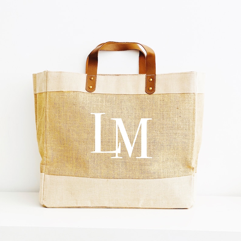 Puede incluir: Una bolsa de lona beige y marr&oacute;n con asas de cuero y un monograma blanco "LM" en la parte delantera.